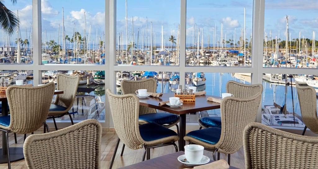 4 tables set for 4 with ocean views of the yacht harbor from the floor-to-ceiling windows at 100 Sails Restaurant & Bar in the Prince Waikiki Hotel.