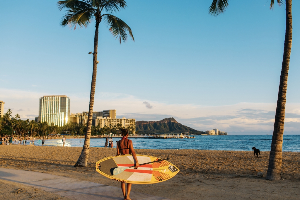 A woman holds a surf board on Waikiki Beach