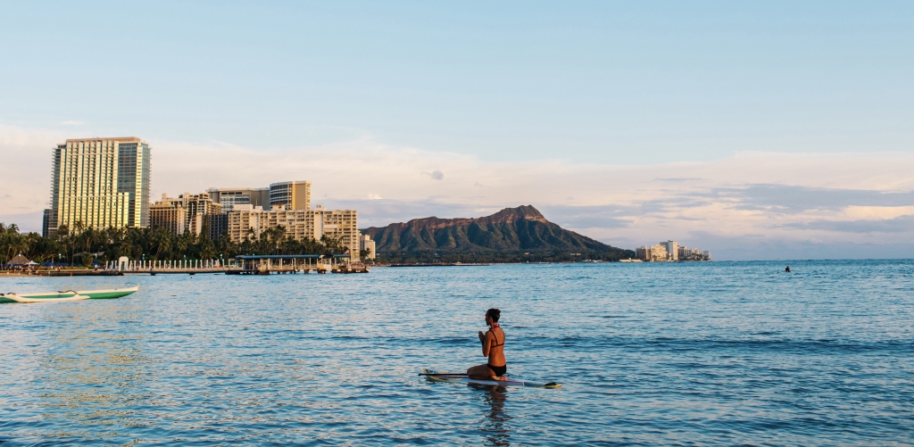 Woman mediating on surfboard at Waikiki Beach with views of Diamond Head.